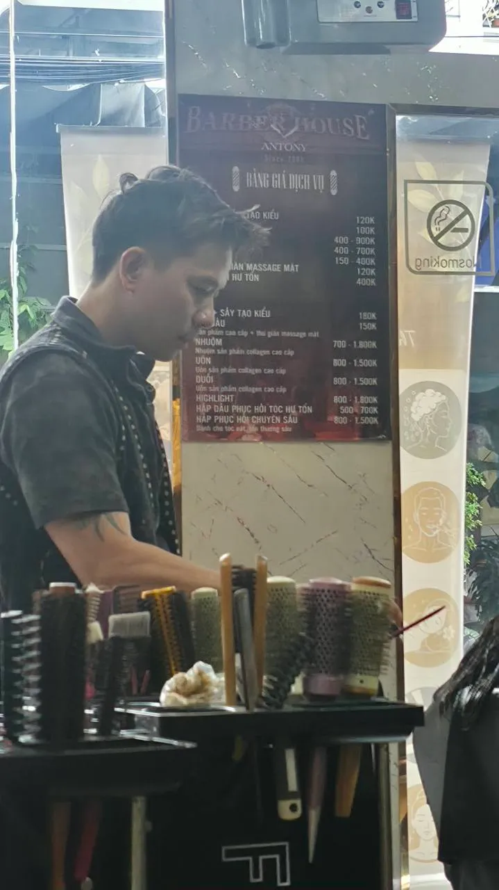 Người thợ đang làm tóc tại Antony, với dụng cụ và bảng giá trong tiệm